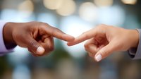 Close up of two diverse hands touching fingers against blurred bokeh background, symbolizing connection, unity and bridging differences in business or social context.
