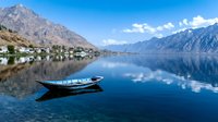 Serene mountain lake with wooden boat reflecting snow-capped peaks and blue sky. Peaceful alpine scenery perfect for travel and nature concepts.