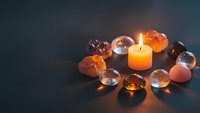 Glowing candle surrounded by colorful healing crystals and gemstones creating peaceful meditation atmosphere for spiritual wellness and relaxation.