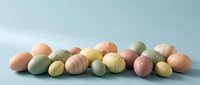 Pastel Easter eggs in soft pink, yellow, green, and peach tones arranged on a light blue background, perfect for spring holiday designs.