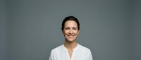 Professional smiling businesswoman in white shirt against gray background for corporate presentations and marketing materials.