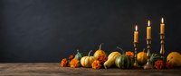 Autumn harvest display with pumpkins, gourds and marigold flowers on rustic wooden table with burning candles against dark textured background for seasonal decor.