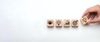 Hand placing wooden blocks with business strategy icons including teamwork, innovation, growth chart and target goal on white background.