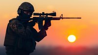 Silhouette of armed tactical operator with rifle and scope against dramatic orange sunset sky, creating powerful contrast and atmospheric mood.