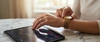 Professional businessman analyzing financial data on tablet and smartphone displaying stock market charts and trading graphs on marble desk.