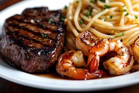 Grilled beef steak and sauteed shrimp served with pasta on white plate, surf and turf dinner with fresh herbs garnish and rich sauce drizzle.
