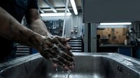Mechanic washing dirty hands with soap in industrial sink after automotive repair work in professional garage workshop.