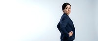 Young South Asian woman in professional navy blazer standing with confident posture, hand on hip, looking over shoulder against white background for corporate and business use.