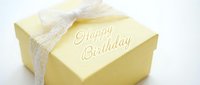 Yellow gift box with Happy Birthday inscription tied with elegant white lace bow on light background, perfect for celebration greeting cards.