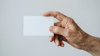 Senior male hand holding blank white business card against neutral background, suitable for corporate branding and professional identity mockups.