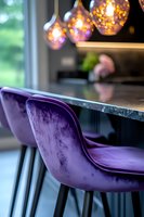 Modern kitchen counter with luxurious purple velvet bar stools and warm pendant lights creating cozy atmosphere. Marble countertop adds elegant touch to interior design.