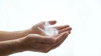 Cupped hands holding glowing crystal diamond with rainbow light reflections against soft white background for luxury jewelry and precious gems concepts.