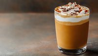 Creamy layered coffee drink topped with whipped cream and chocolate shavings in glass on dark background, selective focus with copy space for menu design.