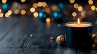 Glowing candle in dark holder with golden Christmas ornament on wooden surface against blurred warm and blue bokeh lights creating cozy festive atmosphere.
