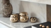 Luxurious metallic gold round ceramic containers on marble counter with decorative vase, modern minimalist home decor styling in neutral tones and textures.