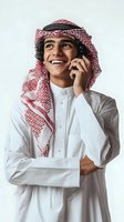 Young Middle Eastern businessman in traditional white thobe and red checkered keffiyeh talking on smartphone with confident smile on neutral background.