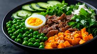 Healthy Buddha bowl with soft-boiled egg, green peas, roasted sweet potato, cucumber slices and fresh herbs on dark plate for nutritious meal planning.