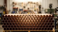 Stack of copper pipes arranged in rows at construction supply warehouse with blurred industrial background for plumbing projects.