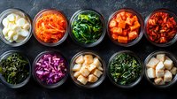 Korean side dishes in glass bowls arranged in rows showing colorful variety of traditional banchan including kimchi, pickled vegetables, and marinated seaweed on dark background.