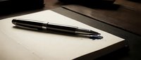 Sleek black pen resting on blank white paper with wooden desk surface, suitable for business, writing, and office design projects.