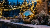 Golden reflective sphere surrounded by frosted evergreen branches and twinkling string lights in evening winter setting, suitable for holiday marketing and seasonal decorations.