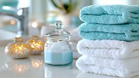 Soft turquoise and white spa towels stacked near glass jar with bath salts, decorated with glowing string lights creating relaxing bathroom atmosphere.
