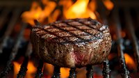 Juicy grilled beef steak with distinctive char marks cooking on flaming barbecue grill. Close-up view captures seared texture and medium-rare doneness against fire background.