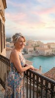 Smiling senior Caucasian woman in floral dress standing on balcony overlooking Mediterranean coastal town at sunset, travel lifestyle.