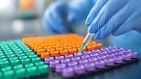 Laboratory technician in blue protective gloves pipetting sample into multicolored plastic test tubes arranged in rows for medical research and diagnostics.