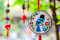 Embroidered ornament featuring blue bird with red flowers in circular hoop, hanging decoration with beaded string and tassel for seasonal decor and crafts.