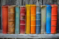 Row of vintage hardcover books in vibrant colors standing on wooden shelf against rustic background, showcasing weathered spines and classic binding styles.
