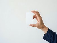 Male hand in dark blue sleeve holding blank white card against neutral background, suitable for business messaging, advertising, and promotional campaigns.