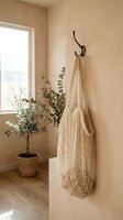 Eco-friendly mesh shopping bag hanging on wall hook in minimalist beige interior with eucalyptus plant for sustainable lifestyle and zero waste living.