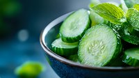 Fresh sliced cucumber with mint leaves in ceramic bowl on dark background. Healthy organic vegetables for salad or spa treatments.