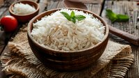 Fluffy white basmati rice garnished with fresh mint in rustic wooden bowl on burlap cloth, surrounded by cooking ingredients on wooden table.
