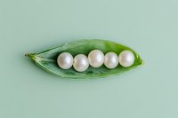Five lustrous white pearls nestled inside an open green pea pod on a soft mint background, creative concept photography.