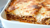 Classic meat lasagna with layers of pasta, ground beef, tomato sauce and melted cheese, baked to golden brown perfection, close up view showing texture and layers.