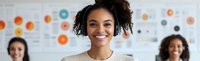 Young African American businesswoman with curly hair and bright smile in office setting, leading diverse team during creative meeting presentation.