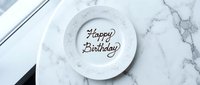 Happy Birthday written in chocolate on a white ceramic plate, placed on a marble surface, elegant celebration concept for greeting cards.