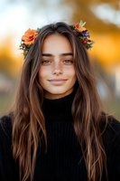 Young woman with floral crown and long brown hair wearing black turtleneck sweater smiles warmly against blurred autumn background. Natural beauty portrait.