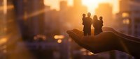 Business team silhouettes standing on open palm against golden city sunset backdrop symbolizing leadership support and corporate mentorship.