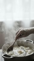 Hand stirring creamy soup in pot with wooden spoon, steam rising from hot homemade meal preparation in rustic kitchen setting for cooking and culinary content.