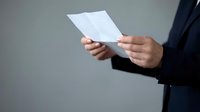 Professional businessman in dark suit holding white document papers for business communication and corporate correspondence review.