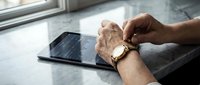 Male hand with luxury gold watch checking time near modern tablet device on marble surface by window for business and lifestyle concepts.