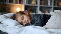 Young child sleeping peacefully in bed with soft lighting and cozy grey bedding, creating tranquil bedroom atmosphere for concepts of healthy sleep, rest and bedtime routine.