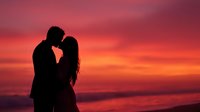 Romantic couple silhouette embracing at sunset beach with dramatic pink orange sky. Love, romance, relationship concept for wedding, Valentine's Day designs.