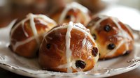 Freshly baked hot cross buns with white icing crosses and raisins on decorative plate, traditional Easter pastry for holiday baking and seasonal celebrations.