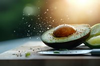 Fresh cut avocado with spices sprinkled in motion against blurred background with sunlight and lime slice, dramatic food photography composition.