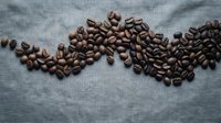 Roasted coffee beans scattered on textured blue fabric background for cafe branding and beverage marketing materials.
