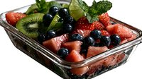 Fresh watermelon chunks mixed with blueberries and kiwi slices in glass container, garnished with mint leaves, close up view of summer fruit salad with water drops.